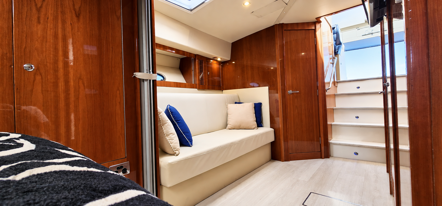 SEADUCTION lower-deck lounge with cream seating, warm timber cabinetry and the bathroom door closed